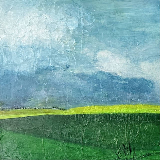 This is an acrylic abstract landscape painting as seen from above. Plots of land are in triangles of various shades of green. The sky is blue with some storm clouds and white clouds. Tiny trees outline the horizon. By Juanita Bellavance